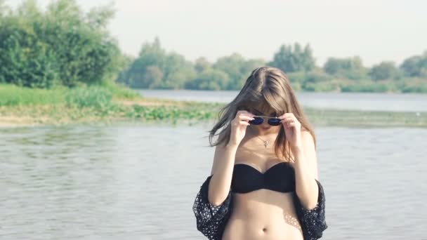 Девушка в воде раздевает солнцезащитные очки и смотрит в камеру. Медленно. — стоковое видео