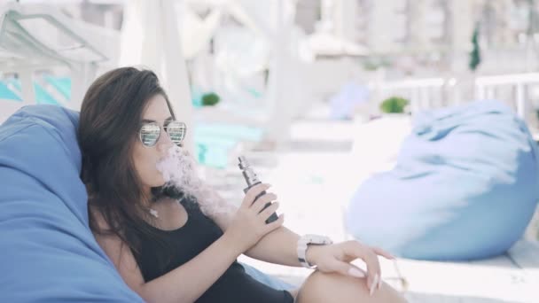 Smart girl in black smoking e-cigarette and resting on the lounge in 4K — Stock Video