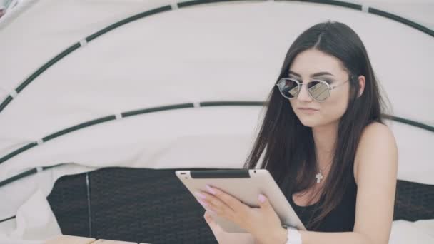 Pretty girl utiliza tableta digital descansando en el salón de playa en 4K — Vídeos de Stock
