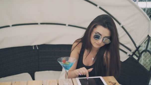 Ragazza alla moda utilizza tablet digitale a riposo sulla spiaggia lounge in 4K — Video Stock