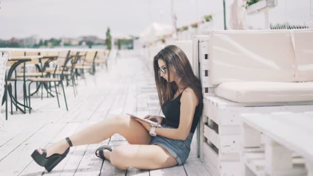 Chica inteligente sentada en los salones de la playa y el uso de la tableta en 4K — Vídeos de Stock
