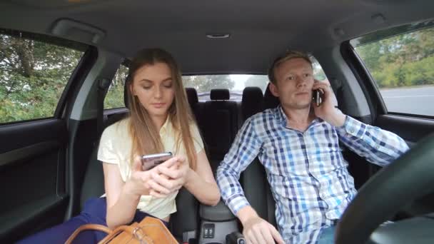 Hombre joven hablando por teléfono y chica usando teléfono inteligente en el coche en 4K — Vídeo de stock