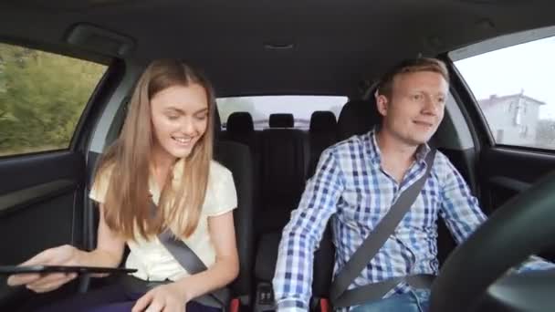 Забавная пара за рулем в машине, улыбаясь и используя планшет 4K — стоковое видео