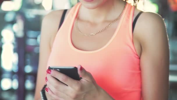 Ragazza che usa il telefono in palestra e sorride su una macchina fotografica. Lentamente. — Video Stock