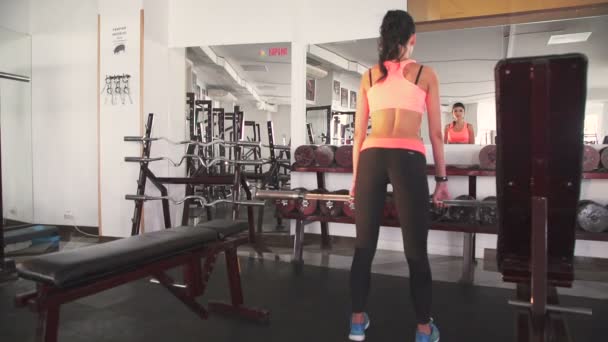 Chica usando barra para ponerse en cuclillas en el gimnasio. Mira atrás. Despacio. — Vídeos de Stock