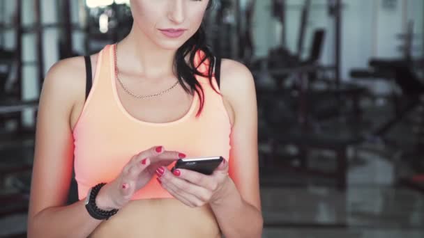 Mujer feliz usando el teléfono en el gimnasio y sonriendo en una cámara — Vídeo de stock