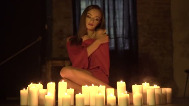 Leidenschaftliches einsames Mädchen sitzt auf dem Boden neben vielen brennenden Kerzen in einem dunklen Raum — Stockvideo