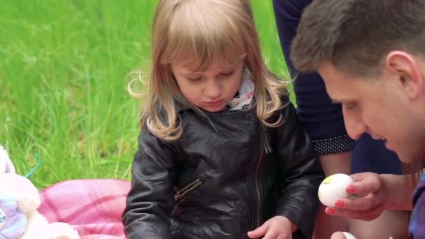 Primer plano de niña con padres pintando huevo de Pascua en un parque — Vídeos de Stock