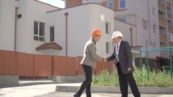 Chiefs in helmets meeting near buildings, shaking hands. 4K — Stock Video