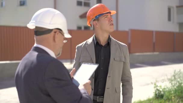 Dos arquitectos están discutiendo en cascos de construcción y usando tableta. 4K — Vídeo de stock