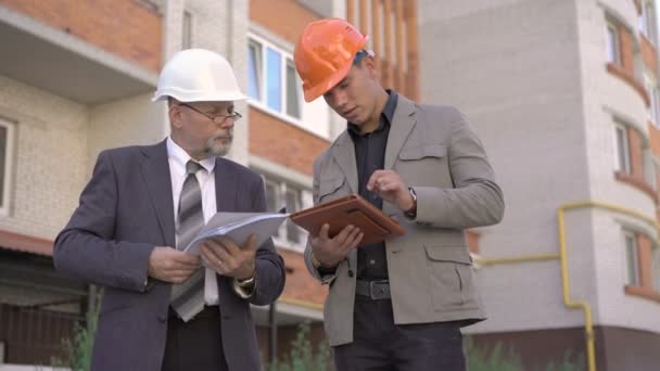 Two business worker in helmet discussing, using tablet near build. 4K — Stock Video