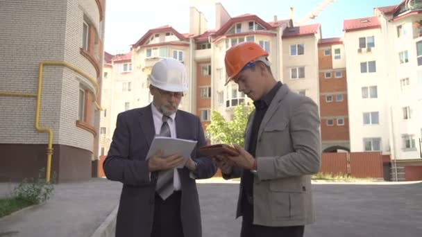 Dos hombres de negocios discutiendo el esquema de construcción cerca de construye. 4K — Vídeo de stock