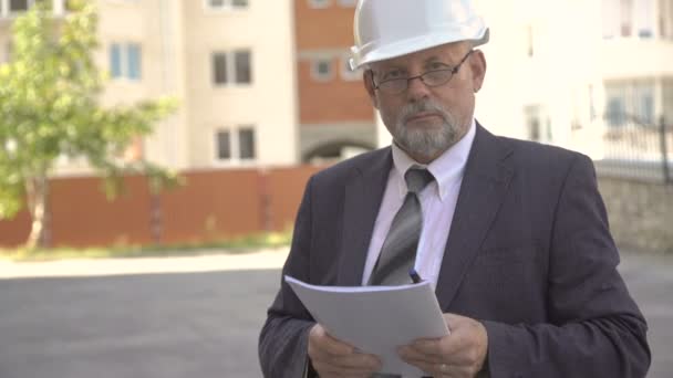 Mature builder in helmet with documents in hands looking on camera. 4K — Stock Video