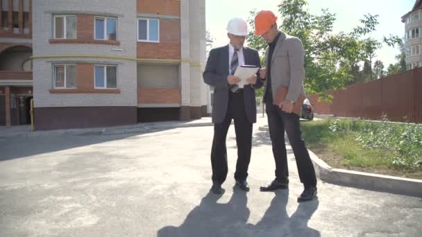 Deux ouvriers regardant sur le plan de la construction près des bâtiments. 4K — Video