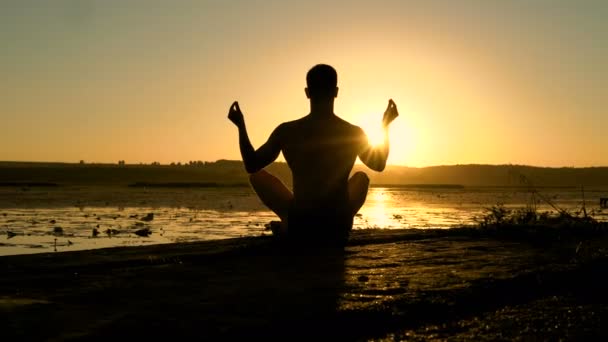 Silueta masculina practicando meditación en la playa al atardecer. 4K — Vídeos de Stock