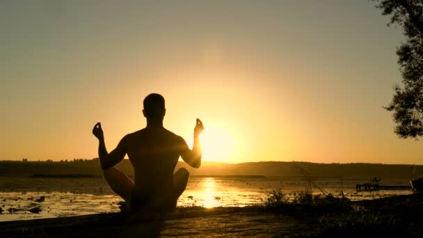 Silhouette eines jungen Mannes, der bei Sonnenuntergang am Strand meditiert. 4k — Stockvideo