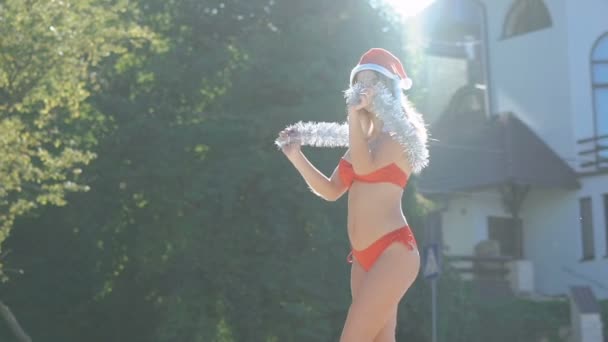 Гламурная девушка в шляпе Санты танцует с рождественским украшением в солнечный день. Медленно. — стоковое видео