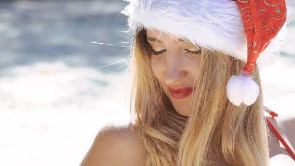 Chica en traje de baño rojo y sombrero de santa coqueteando y posando en la playa. Despacio. — Vídeo de stock