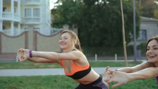 Две девушки делают активные упражнения с улыбкой на лицах на траве. 4K — стоковое видео