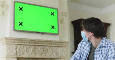 Uzun izolasyondan yorulmuş bir adam televizyonda seyrediyor ve kötü istatistiklerden başını sallıyor.