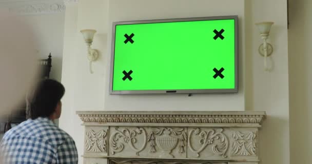 緑の画面でテレビのプラズマを見ている男、リモコンでチャンネルを切り替える — ストック動画