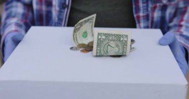 Eldivenli bir erkek, kameraya üzerinde biraz para olan bir teslimat kutusu taşıyor.