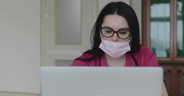 L'infirmière en lunettes, masque de protection et avec phonendoscope travaillant avec ordinateur portable — Video