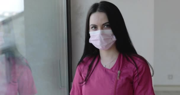 Enfermeira cansada em forma protetora olhando para a câmera, em seguida, inclina-se para janelas manchadas — Vídeo de Stock