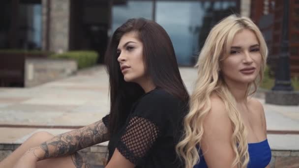 Sexy Brünette und Blondine mit langen Haaren posieren auf der Treppe eines Luxushauses. 4K — Stockvideo
