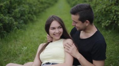 Sevimli bir çift çimenlerde oturuyor, sarılıyor ve öpüşüyor.