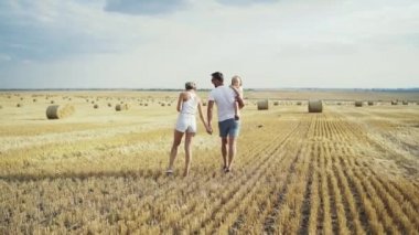 Kucaklaşan kızıyla birlikte geniş bir alanda yürüyen genç bir ailenin arka planı.