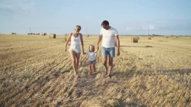 Mutlu ebeveynler kızlarının elini tutar, koşar ve büyük bir yaz tarlasına saman atarlar.