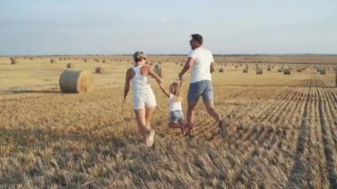 Mutlu ebeveynler kızlarıyla sahada el ele koşar. 4K