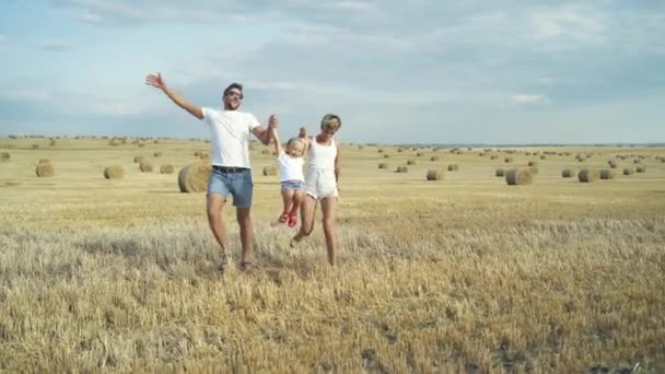 Boldog szülők fogják a lányuk kezét és futnak egy hatalmas nyári mezőn. — Stock videók