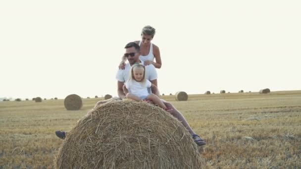 Padres felices con hija pequeña relajándose en un enorme pajar en el campo — Vídeos de Stock