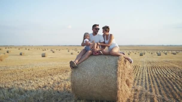 Famiglia felice con il loro bambino che si rilassa nelle carezze sul fieno nel campo — Video Stock