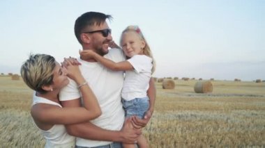 Bir tarlada kameraya gülümseyen neşeli aile portresi.