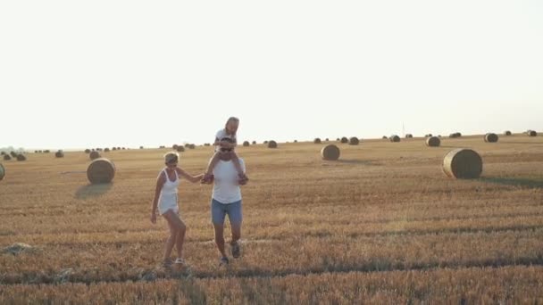 Preciosa familia con niña sobre hombros corriendo en campo espacioso — Vídeos de Stock