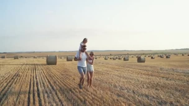 Geniş tarlalarda koşan, küçük omuzlarında küçük bir kızla sevimli bir aile. — Stok video