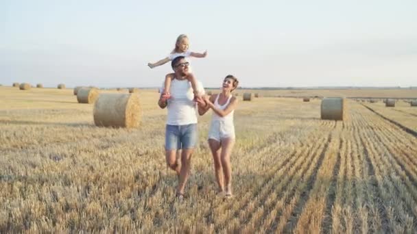 Alegre familia caminar en el campo, chica en los hombros padres muestra pulgar — Vídeos de Stock