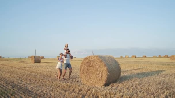 Glückliche Familie mit kleiner Tochter rollt Heuhaufen in sonnigem Feld — Stockvideo