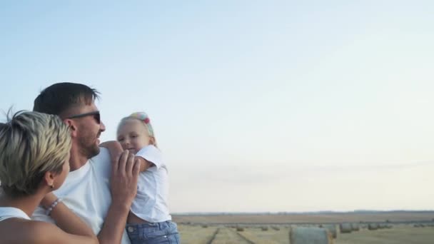 Preciosa familia en abrazos divirtiéndose con la pequeña hija en un campo — Vídeos de Stock