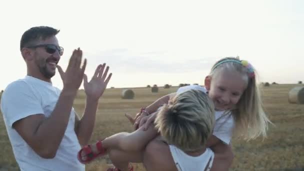 Lycklig mamma och pappa leker med sin dotter och kysser henne på fältet — Stockvideo