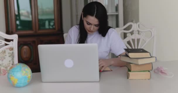 一个漂亮的女学生，带着笔记本电脑和书本在房间里吃饭 — 图库视频影像