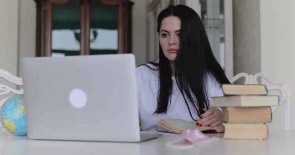 Привлекательная студентка отмечает сборник с ноутбука за столом в комнате — стоковое видео
