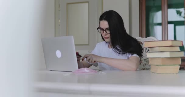 Diligente ragazza in occhiali che studia, annota e digita sul computer portatile a tavola in camera — Video Stock
