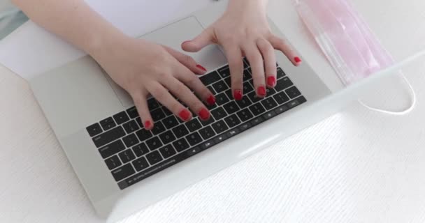 Vista de las manos femeninas escribiendo en el teclado del ordenador portátil en la máscara médica en la mesa blanca — Vídeos de Stock