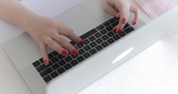 Haut des mains féminines tapant sur le clavier de l'ordinateur portable au masque médical sur le lieu de travail blanc — Video