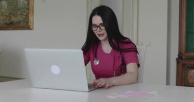 The nurse in glasses advises patients online on laptop in home