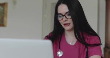 Confident doctor in glasses advises patients online on laptop in home